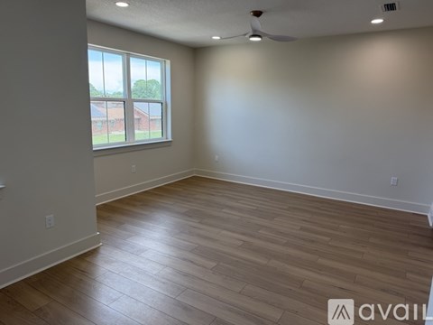 A room with wooden flooring and a window overlooking a red building.