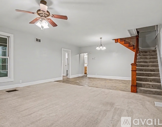 A spacious room with a ceiling fan and a staircase.