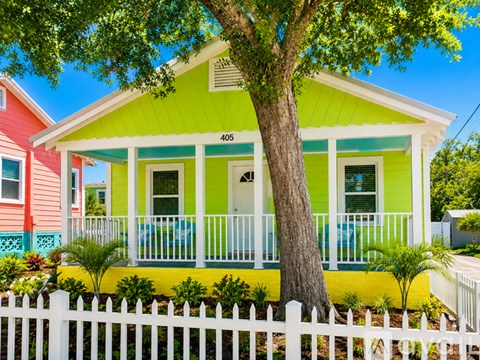 A green house with a white picket fence in front.