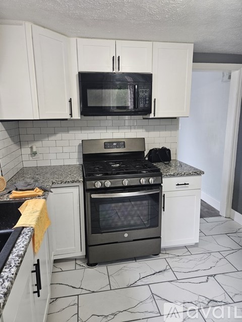 A kitchen with a black microwave above a stove and white cabinets.
