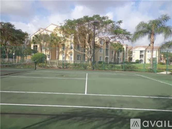 A tennis court is in front of a building with trees.