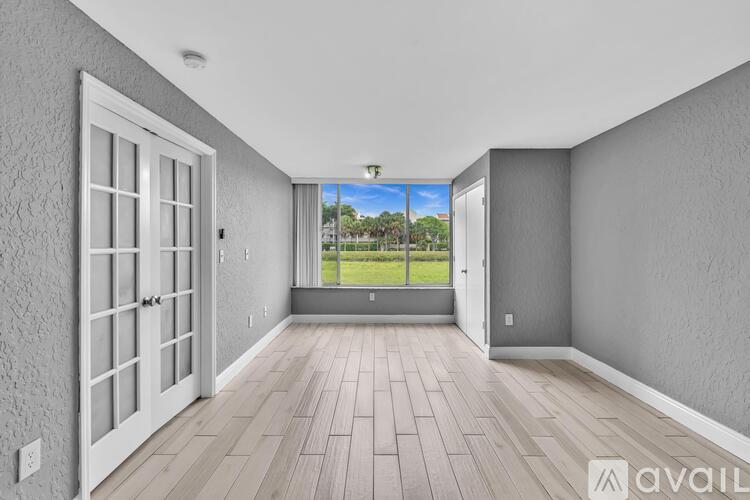 A room with a view of a lawn and trees through a window.