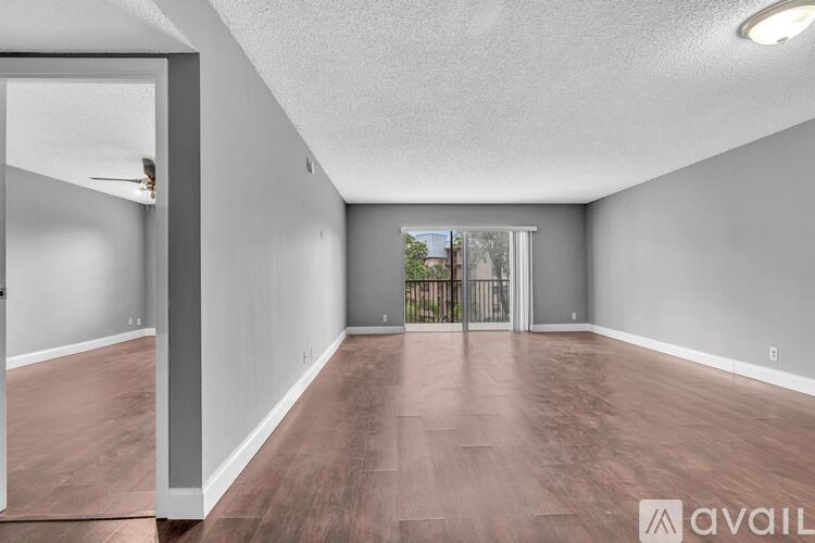 A spacious room with wooden flooring and a sliding glass door leading to a balcony.