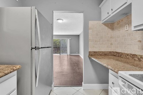 A kitchen with a refrigerator, oven, and a counter with a granite countertop.