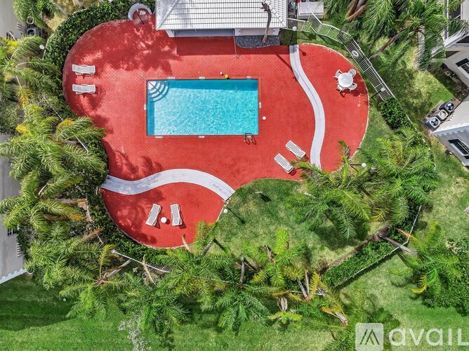 A red swimming pool surrounded by greenery and a white fence.