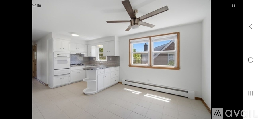 A modern kitchen with white cabinets and a ceiling fan.