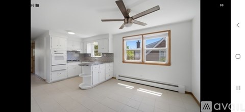 A modern kitchen with white cabinets and a ceiling fan.