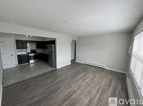 A spacious room with a kitchen area in the background and a large empty space in the foreground.