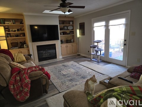 A cat sits on a couch in a living room with a fireplace and a television.