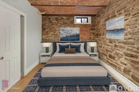 A bedroom with a stone wall and a bed with a blue and beige comforter.