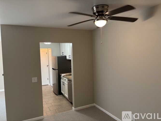 A room with a ceiling fan and a kitchen area in the background.