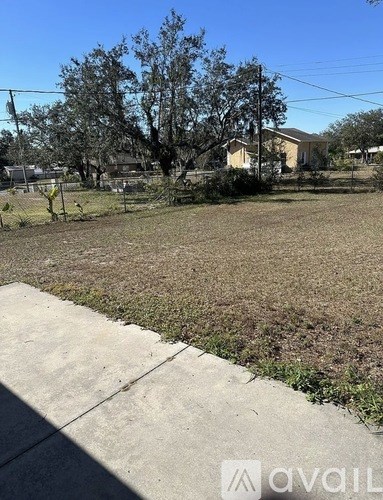 A grassy area with a sidewalk and a house in the background.