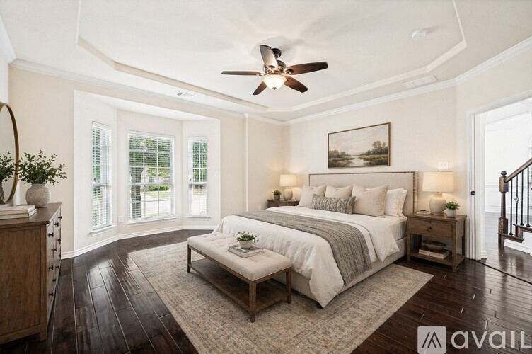 A bedroom with a large bed, a ceiling fan, and a painting on the wall.
