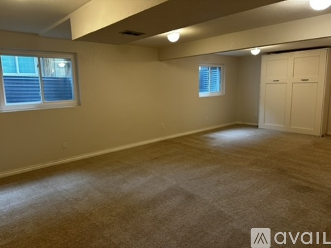 A spacious room with a carpeted floor, two windows, and a door.