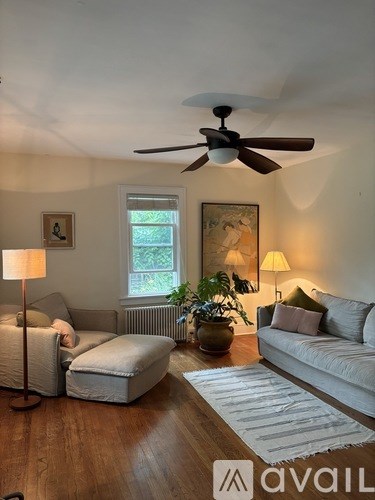 A living room with a white couch, a brown rug, a ceiling fan, and a painting on the wall.