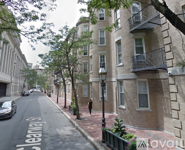 A street view of a residential area with apartment buildings on the right and a tree-lined street on the left.