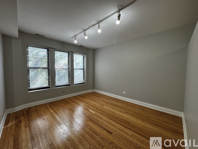 A room with wooden flooring and three windows.