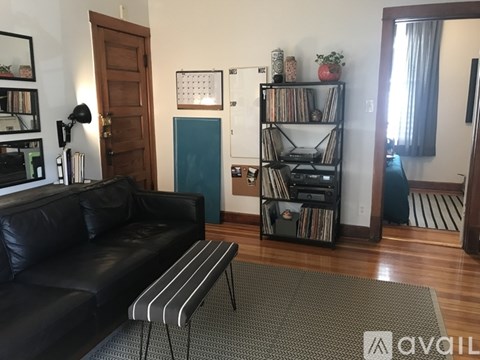 A living room with a black leather couch and a grey rug.