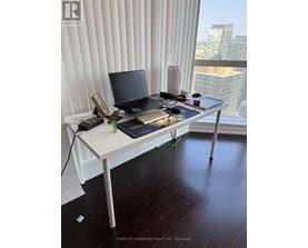 A laptop and a tablet are on a desk in front of a window with blinds.