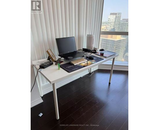 A laptop and a tablet are on a desk in front of a window with blinds.