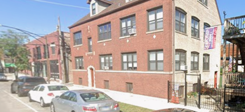 A red brick building with a white car parked in front.