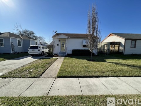 A white car is parked in front of a house with a tree in front of it.