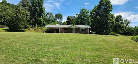 A house is available for sale in a grassy field with trees in the background.