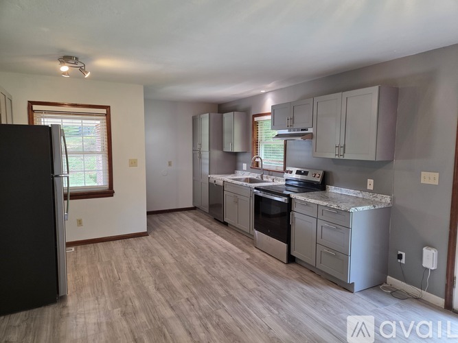A kitchen with a black refrigerator and wooden flooring.