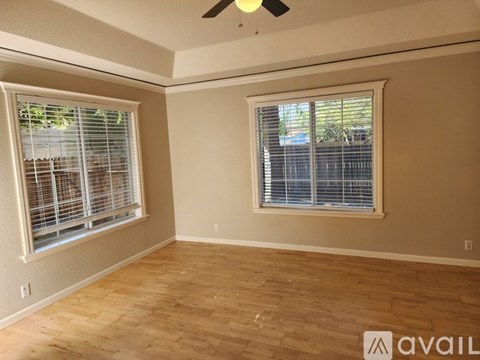 A room with a ceiling fan and two windows with blinds.