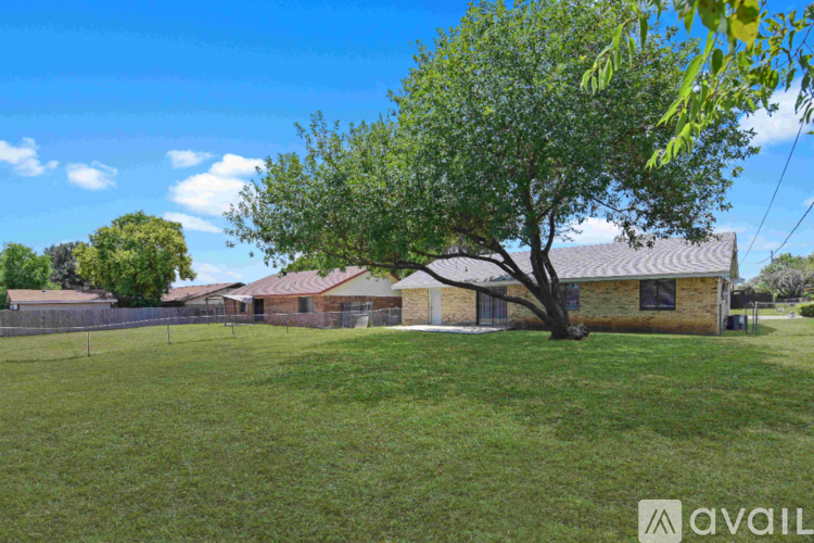 A tree in a grassy field with houses in the background.