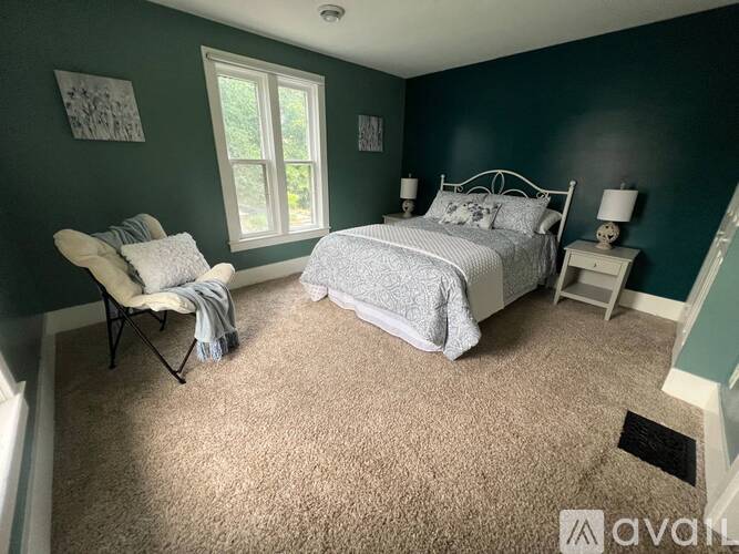 A bedroom with a bed, chair, and window.