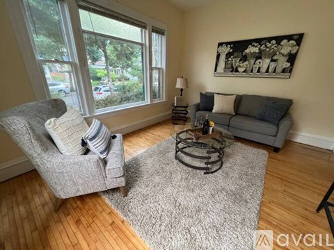 A living room with a grey couch, a grey chair, a grey rug, and a painting on the wall.