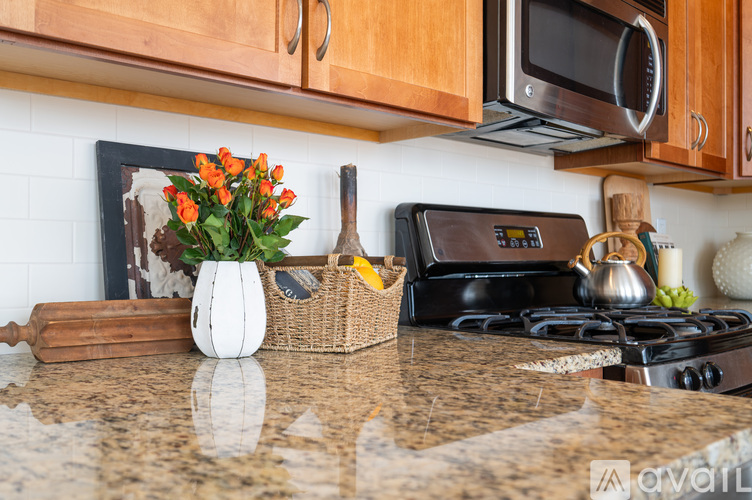 A kitchen counter with a white vase of flowers, a rolling pin, a basket, and a black stove top.