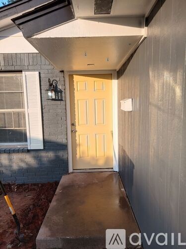 A small white house with a yellow door and a shovel in the front yard.