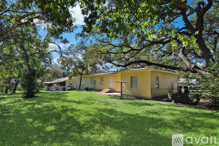 A yellow house with a green lawn and trees in the background.
