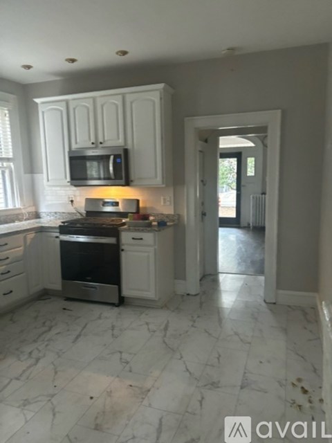 A kitchen with white cabinets and marble flooring.