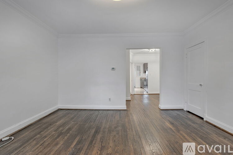A room with wooden floors and white walls, with a doorway leading to another room.