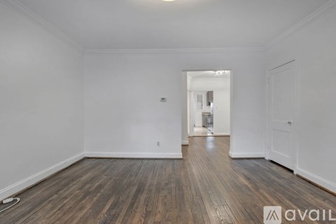A room with wooden floors and white walls, with a doorway leading to another room.