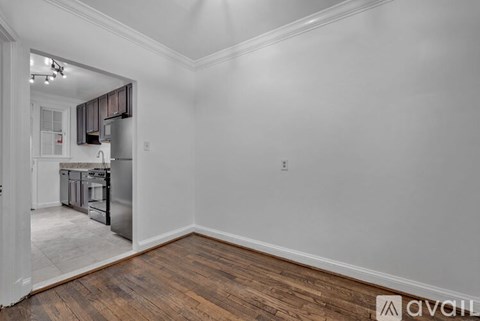 A room with wooden floors and white walls, leading to a kitchen area.