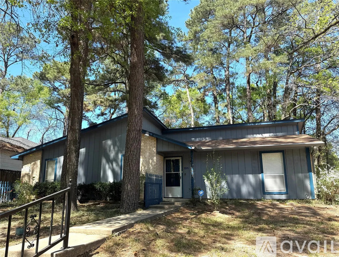 A house with a grey roof and a blue door is surrounded by trees.