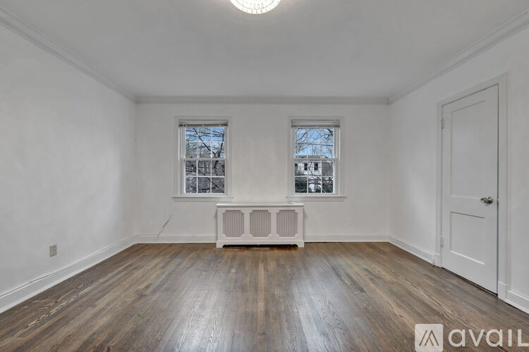 A room with wooden floors and two windows with white radiators beneath them.