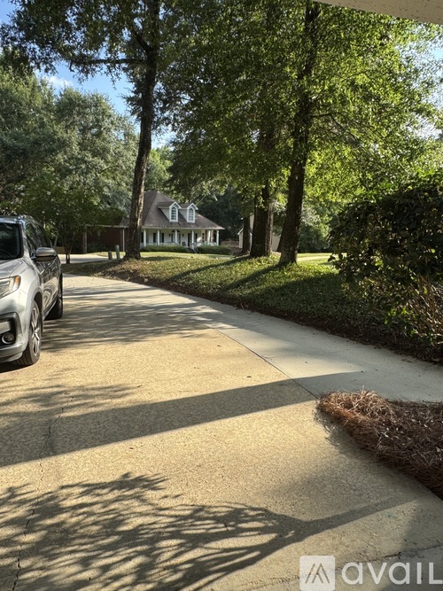 A car is parked on a driveway with a house and trees in the background.