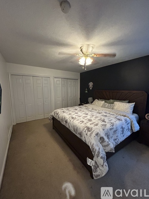 A bedroom with a bed, ceiling fan, and a wall hanging.