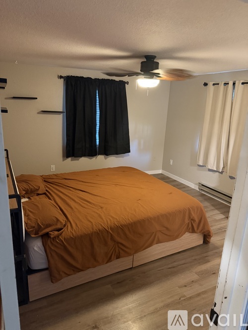 A bedroom with a bed covered in an orange sheet set in a corner of the room.