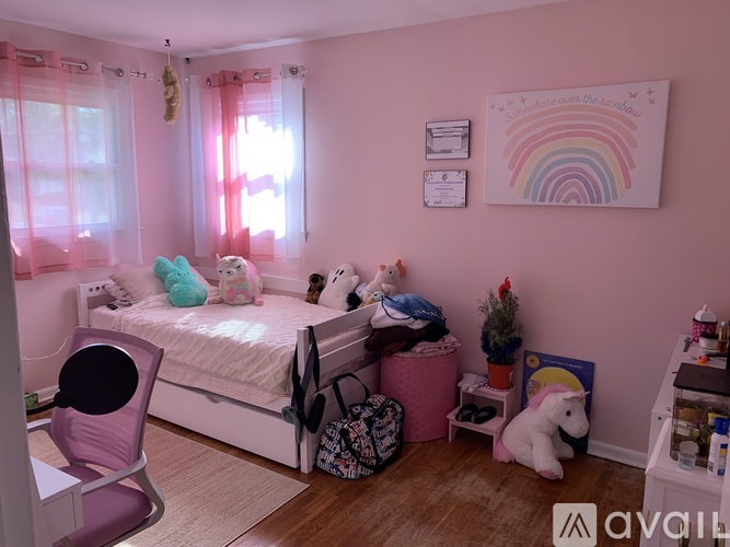 A child's bedroom with a white bed, pink walls, and a rainbow poster.