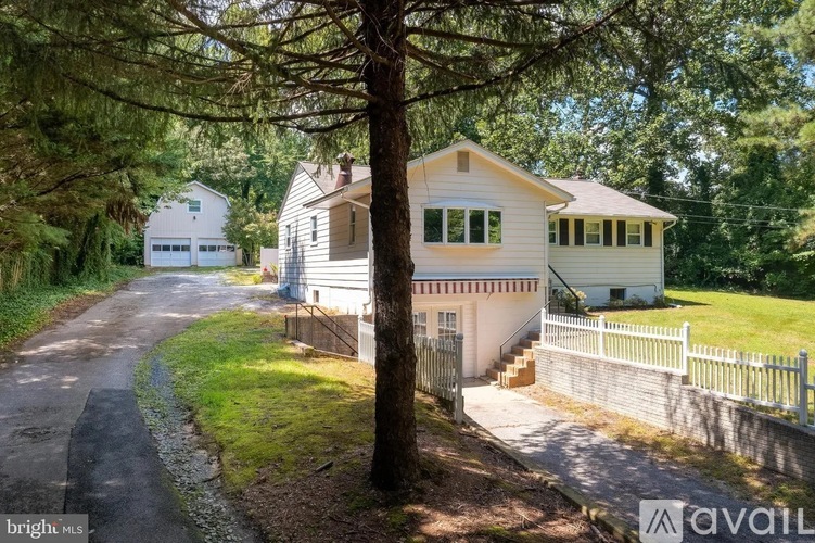 A house with a white exterior is surrounded by a white picket fence and a tree in front of it.