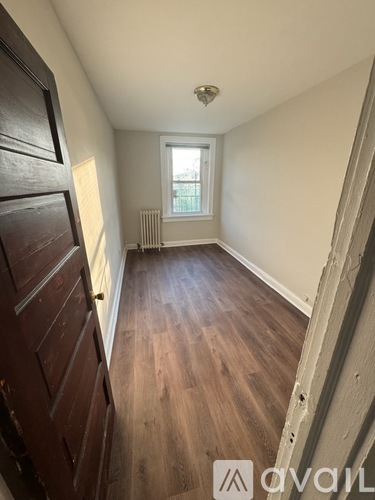A room with wooden floors and a window with a view of a fence and trees.