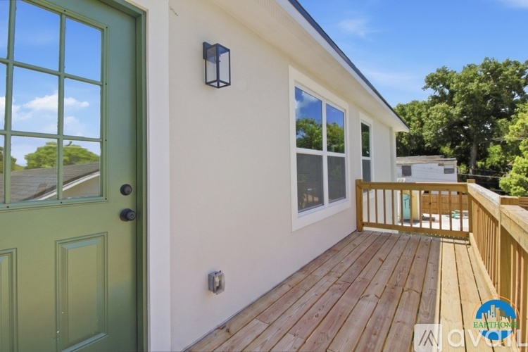 A green door is on the left of a white building with a wooden deck.