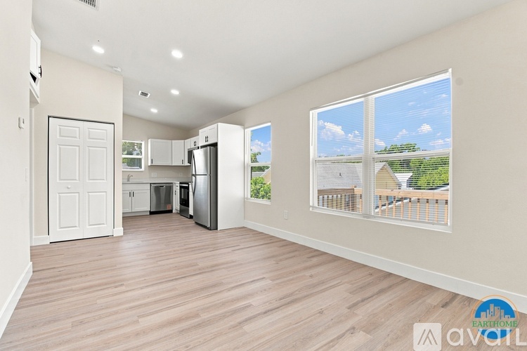 A spacious, empty room with wooden floors and a large window showing a view of a house and trees.