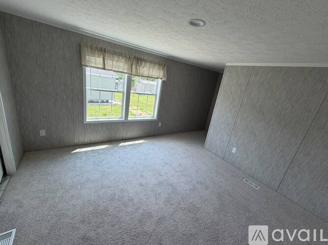 A room with grey carpet and a window with a view of a fence and trees.